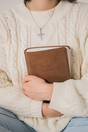 close-up-of-person-wearing-cross-necklace-with-bible-in-arms